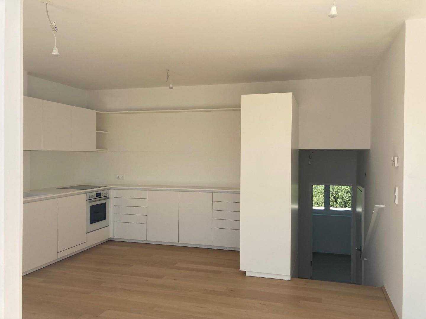 Helle, leere Küche mit weißen Einbauschränken und Holzboden, bereit für die Installation von Geräten.