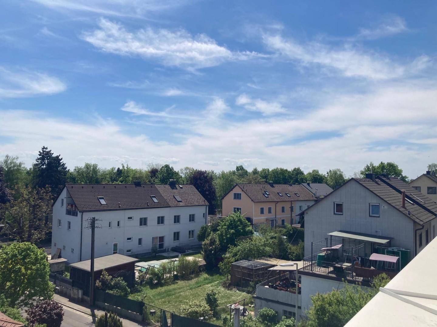 Weitläufiger Blick über eine Wohnsiedlung mit Gärten und Bäumen unter einem hellblauen Himmel.