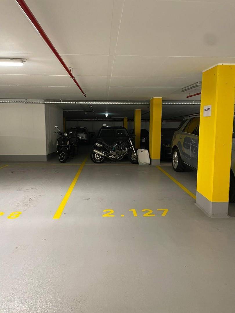 Saubere Tiefgarage mit mehreren Fahrzeugen und klar gekennzeichneten Parkplätzen sowie gelben Stützpfeilern.