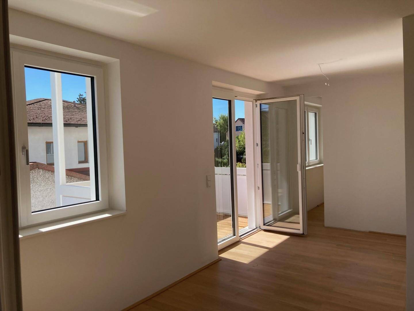 Helles Zimmer mit Holzboden und Zugang zu einem Balkon, der viel Sonnenlicht hereinlässt.