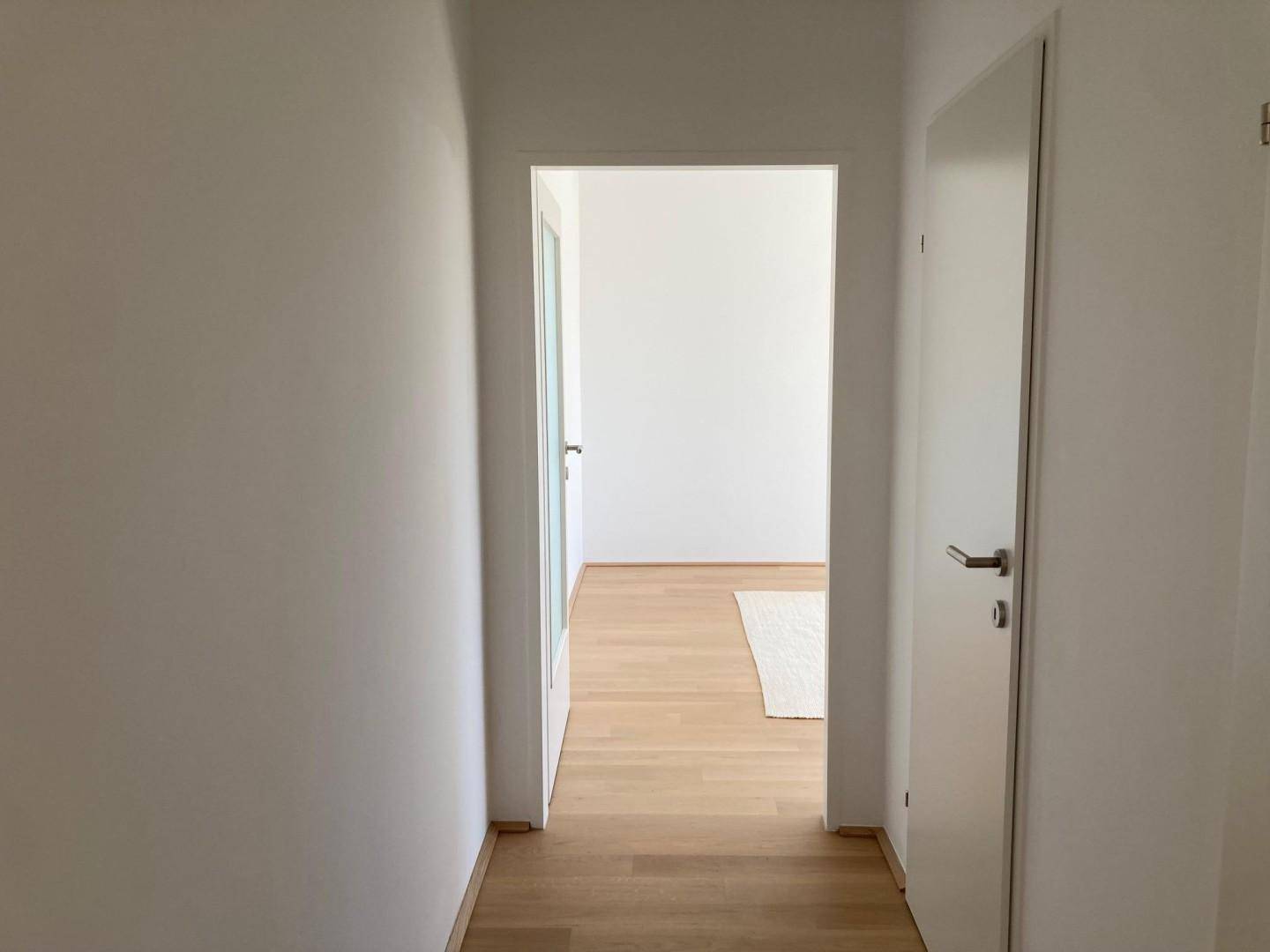 Heller Flur mit Holzboden und weißen Türen, der zu einem weiteren Zimmer führt.