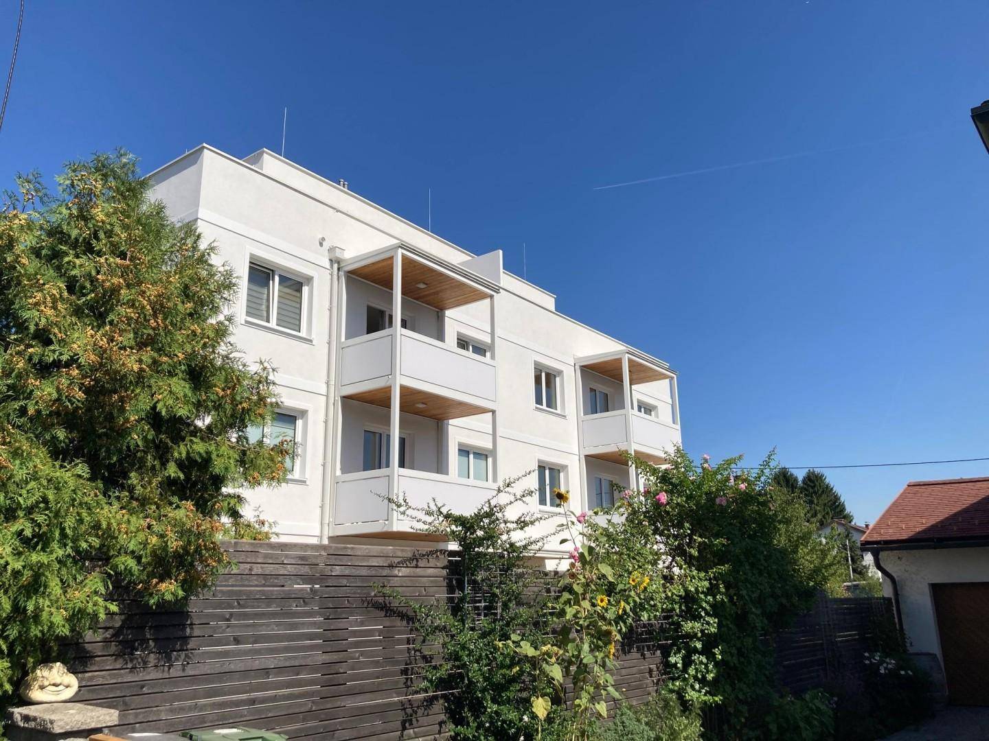 Modernes Mehrfamilienhaus mit weißer Fassade und mehreren Balkonen unter blauem Himmel.