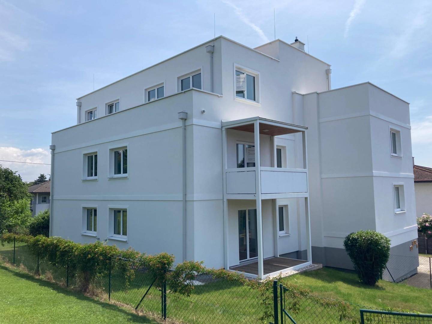 Modernes Mehrfamilienhaus mit weißer Fassade, großen Fenstern und Balkonen.