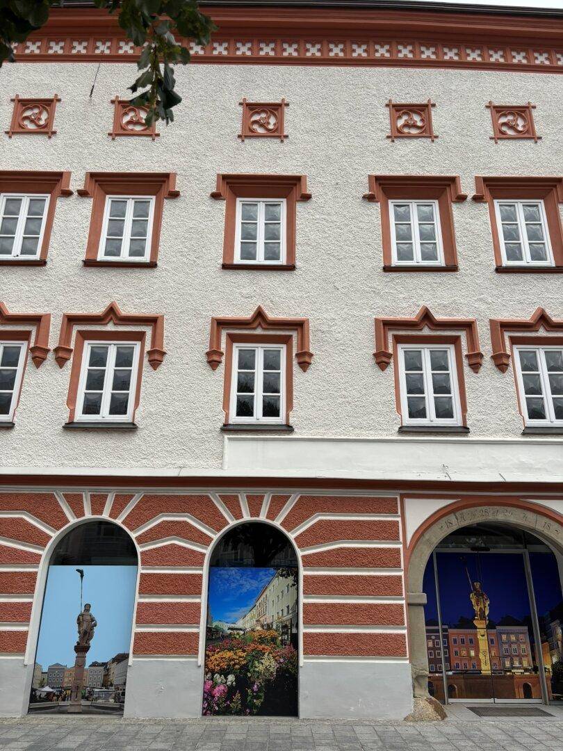 Gesamte Fassade des historischen Gebäudes mit kunstvollen Verzierungen und Schaufenstern im Erdgeschoss.