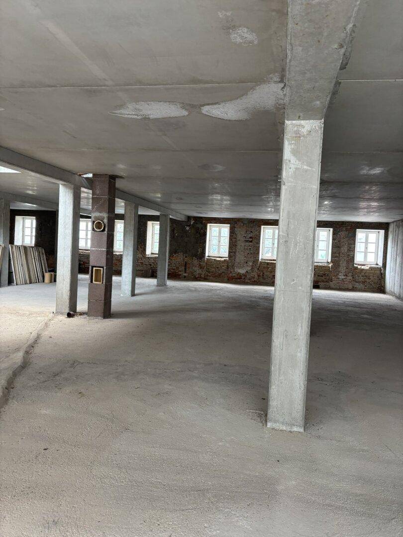 Großer Rohbau mit Betonstützen, unverputzten Ziegelwänden und vielen Fenstern.