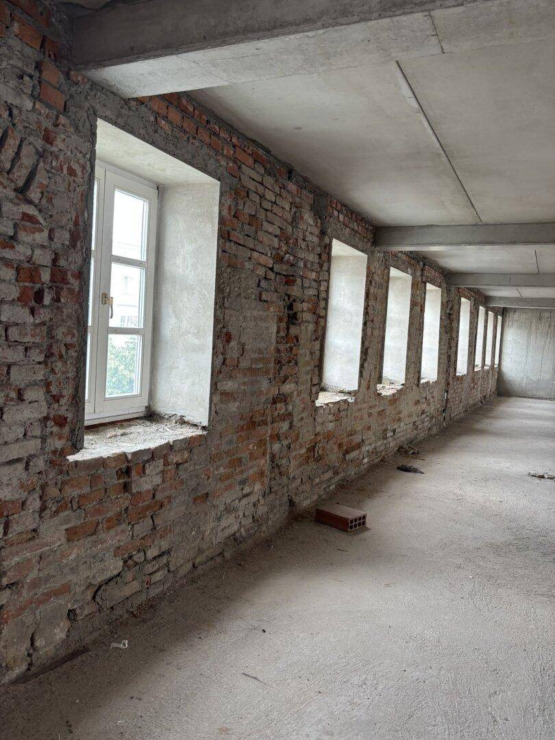 Lange unverputzte Ziegelwand mit mehreren Fenstern in einem Rohbau.