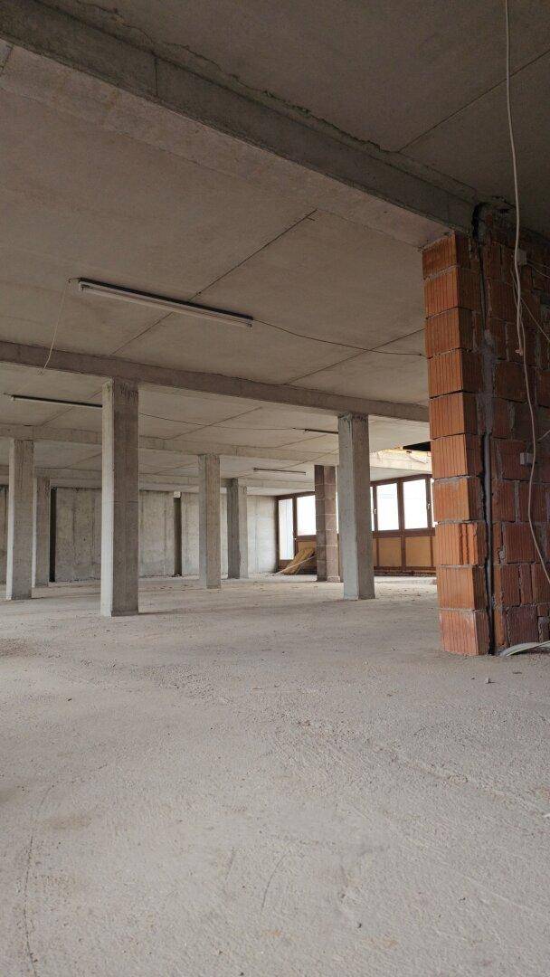 Rohbau eines Innenraums mit Betonstützen, unverputzten Ziegelwänden und Fenstern.
