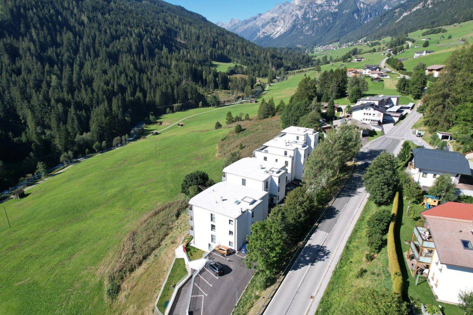 Moderne Wohngebäude entlang einer Straße mit Parkplätzen und weitem Blick ins Tal.