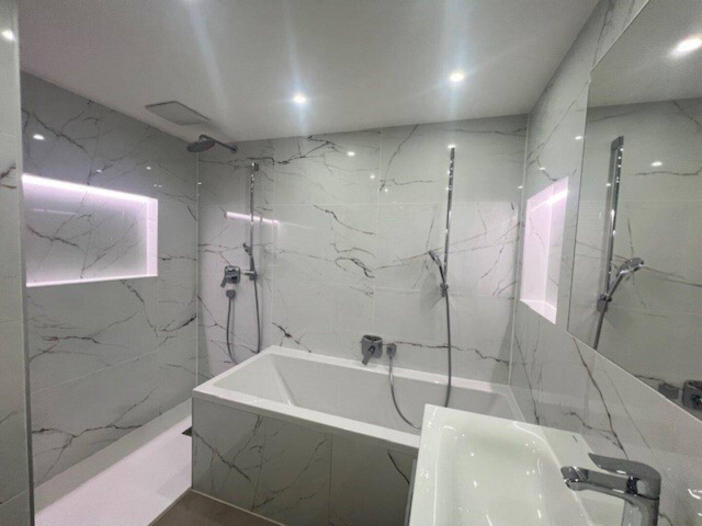 Modernes Badezimmer mit Badewanne, Dusche und eleganten Fliesen in Marmoroptik.