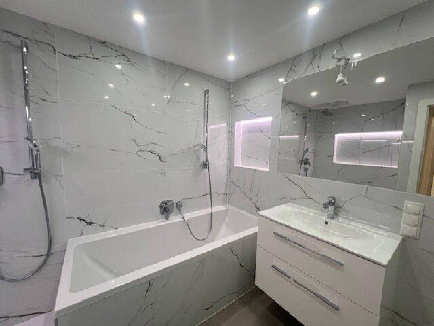 Stilvolles Badezimmer mit Badewanne, Dusche, Waschtisch und integrierter Spiegelbeleuchtung.