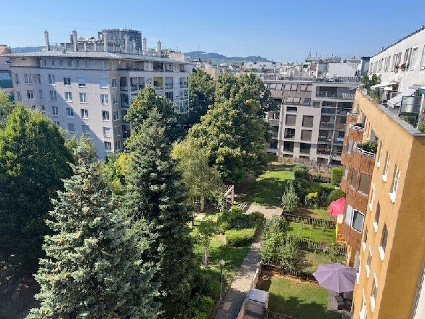 Blick auf einen grünen Innenhof mit Spielplatz, umgeben von Wohngebäuden in urbaner Umgebung.