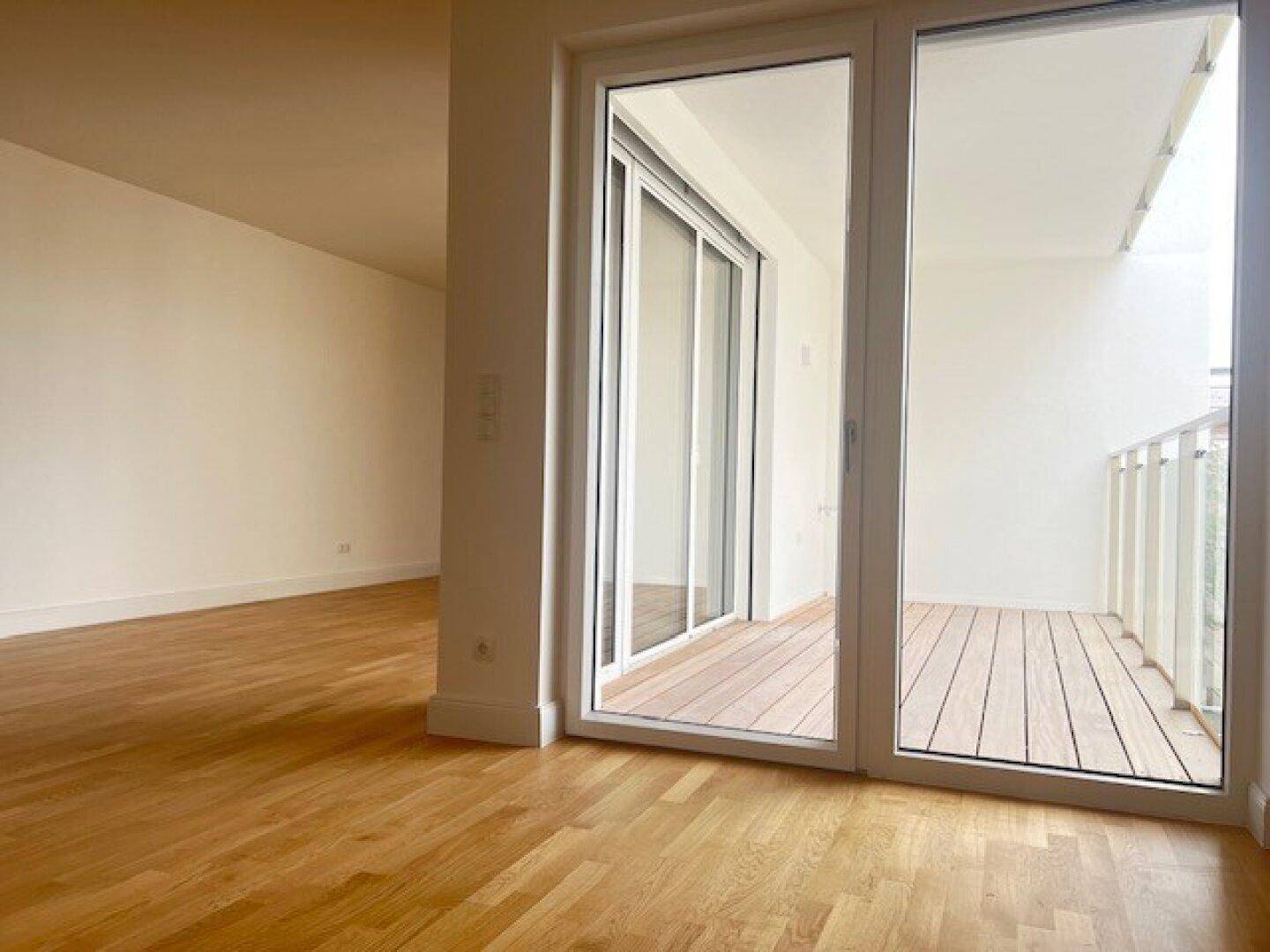 Heller, leerer Raum mit Eichenparkettboden und großen Schiebetüren zum Balkon.