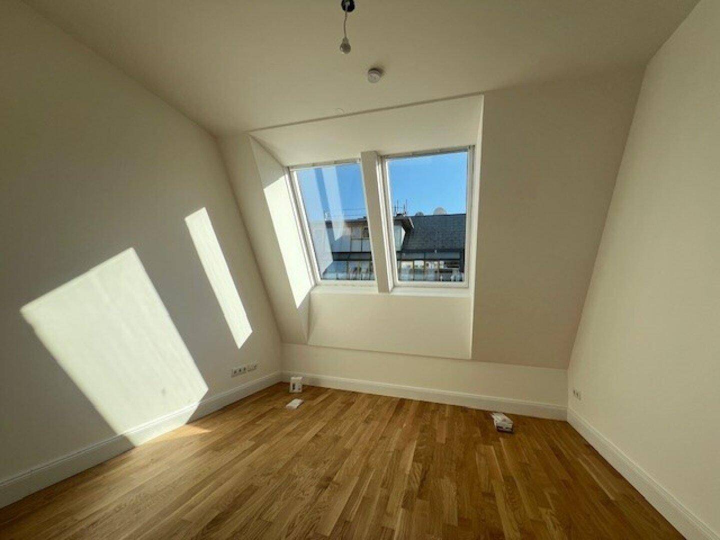 Geräumiger, heller Raum mit Holzboden und schrägen Wänden, beleuchtet durch zwei Dachfenster.
