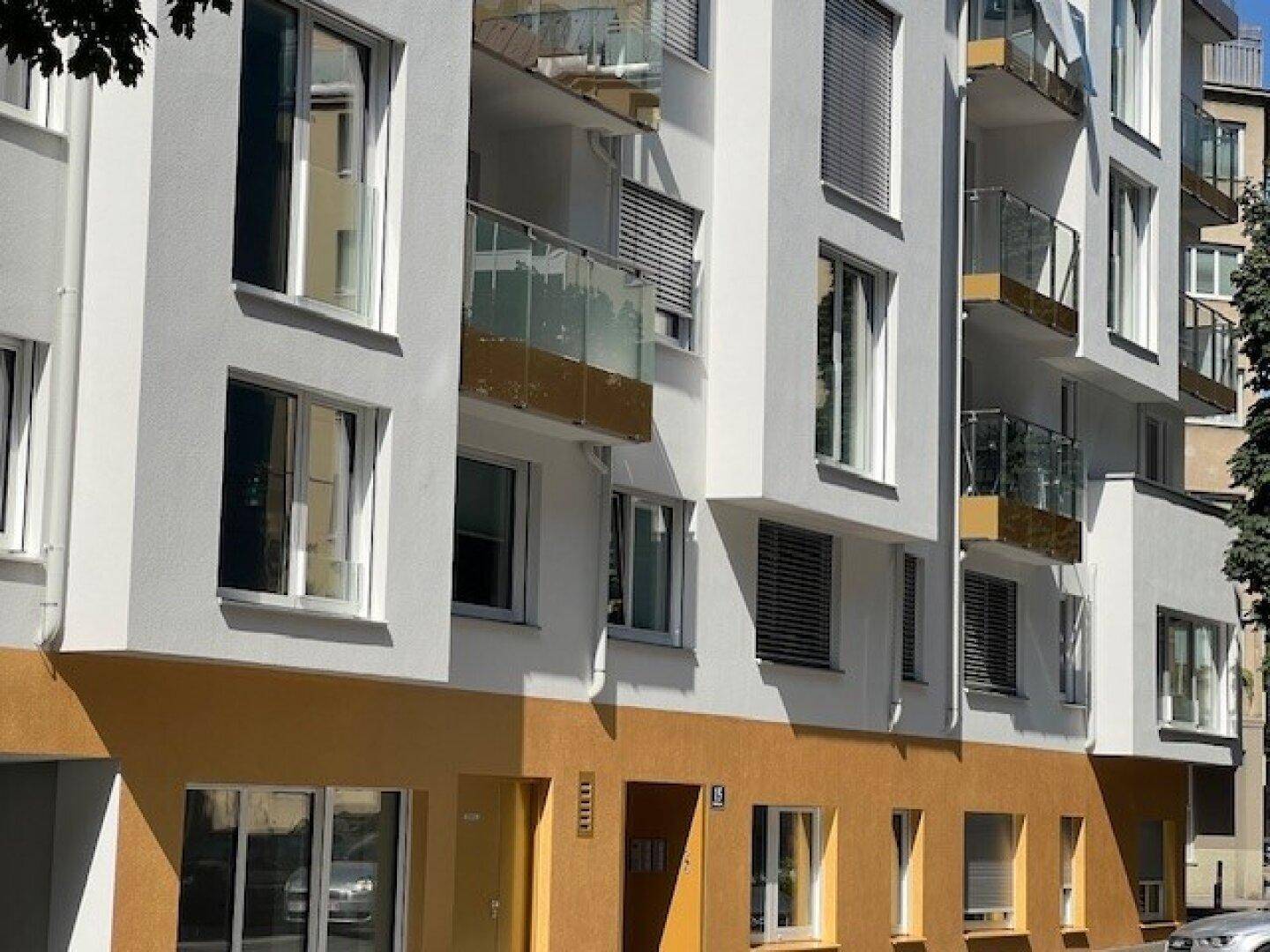Moderne Gebäudefassade mit weißen Wänden, gelben Akzenten und mehreren Balkonen.