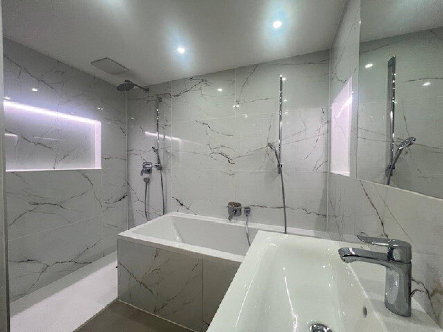 Modernes Badezimmer mit großformatigen Fliesen in Marmoroptik, Badewanne und Dusche.