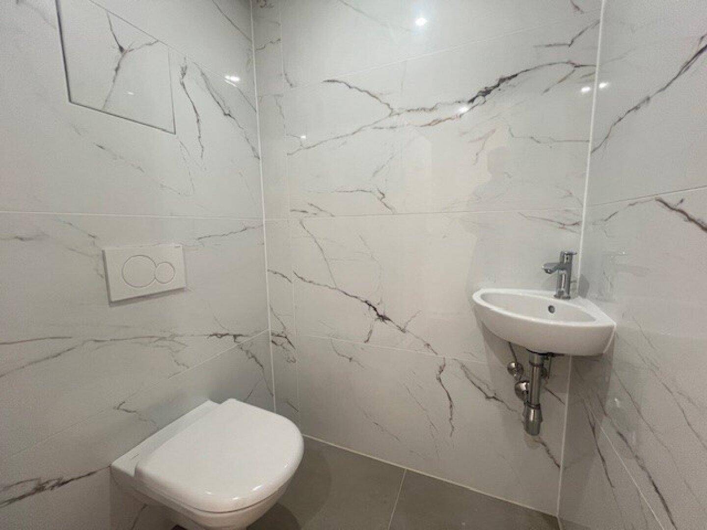 Modernes Gäste-WC mit wandhängendem WC und kleinem Waschbecken, gefliest in Marmoroptik.