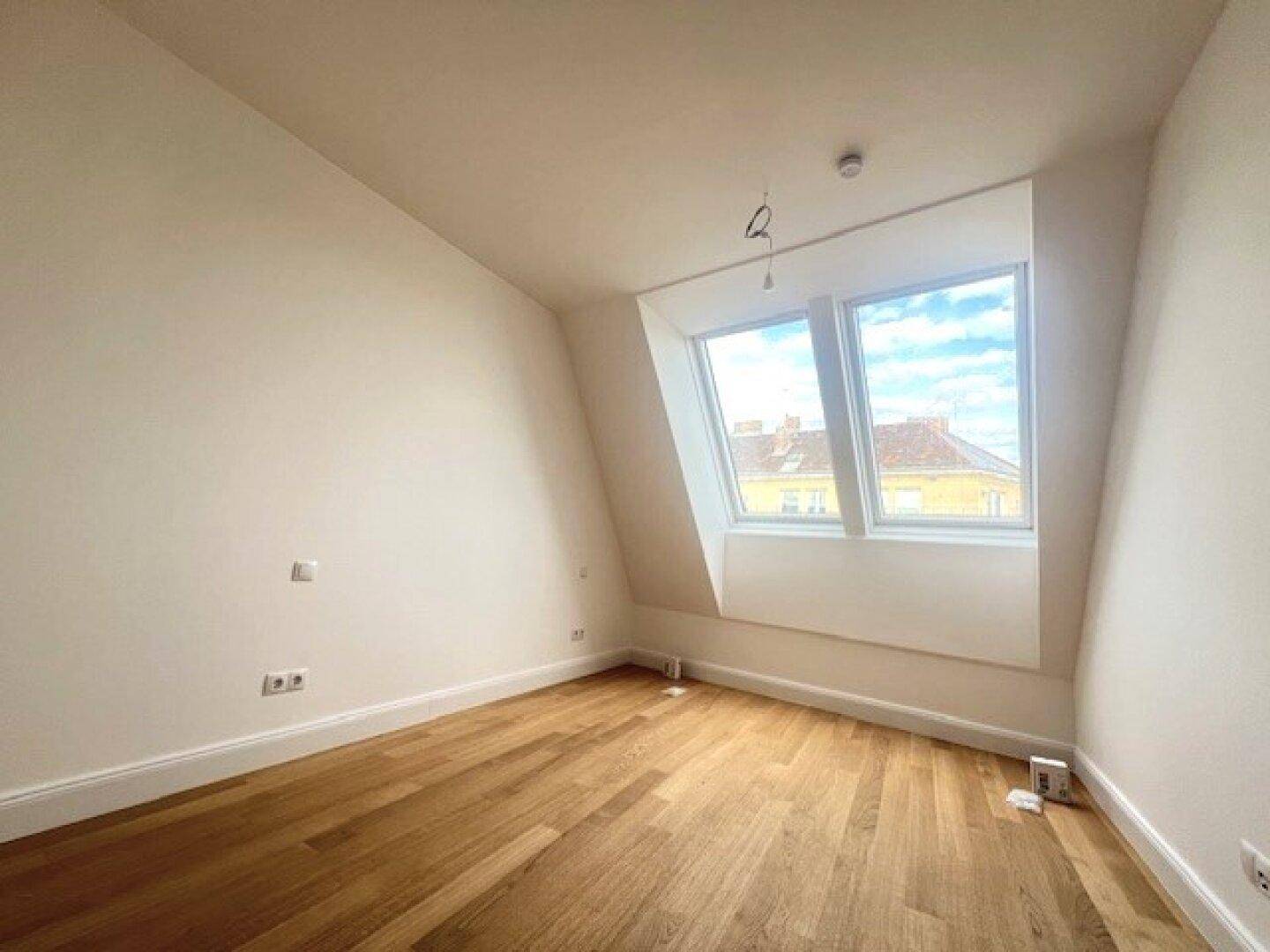 Helles Dachgeschosszimmer mit Holzboden, schräger Decke und zwei Dachfenstern.