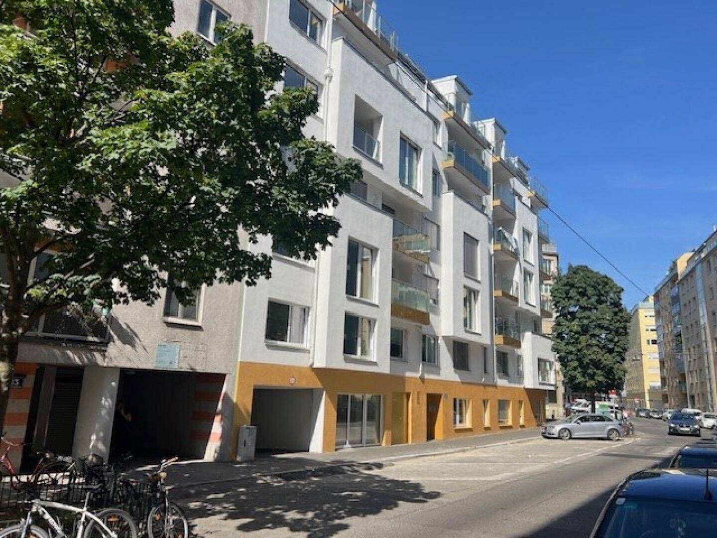 Moderne Fassade eines Wohngebäudes mit weißen Wänden, Balkonen und großen Fenstern an einer Straße.