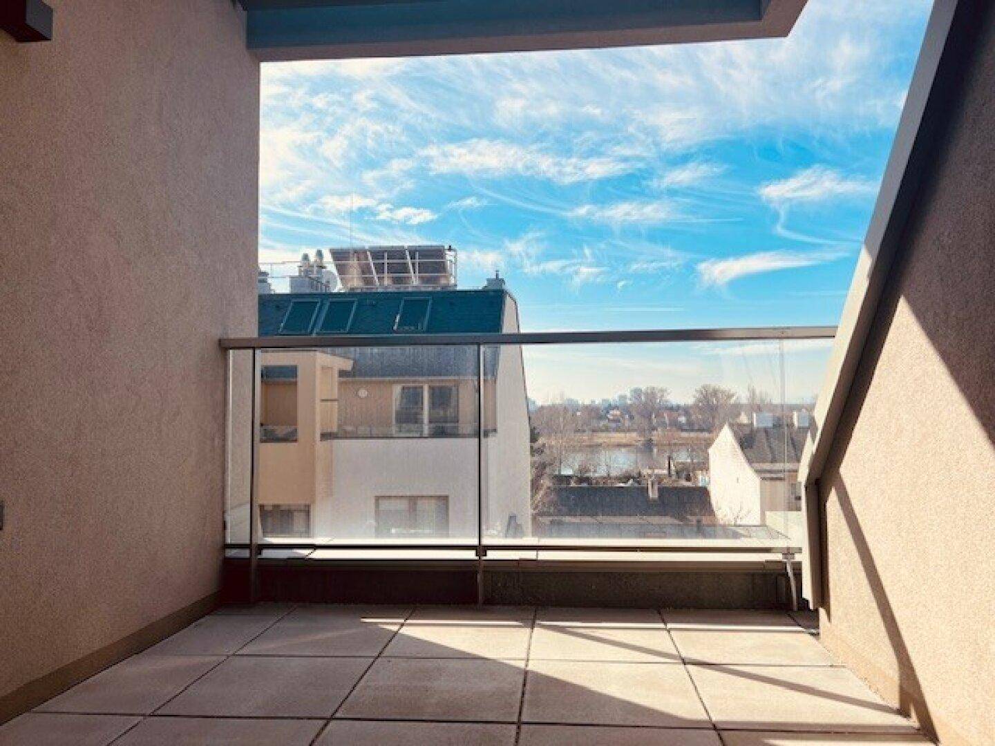 Heller Balkon mit Fliesenboden und Glasbrüstung, bietet einen weiten Blick auf die Umgebung.