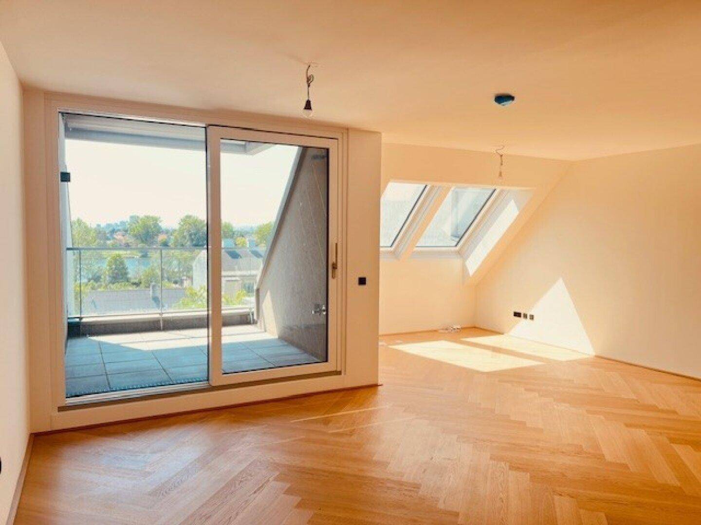 Helles Zimmer mit Fischgrätparkett, Zugang zum Balkon und Dachfenstern, bietet viel natürliches Licht.