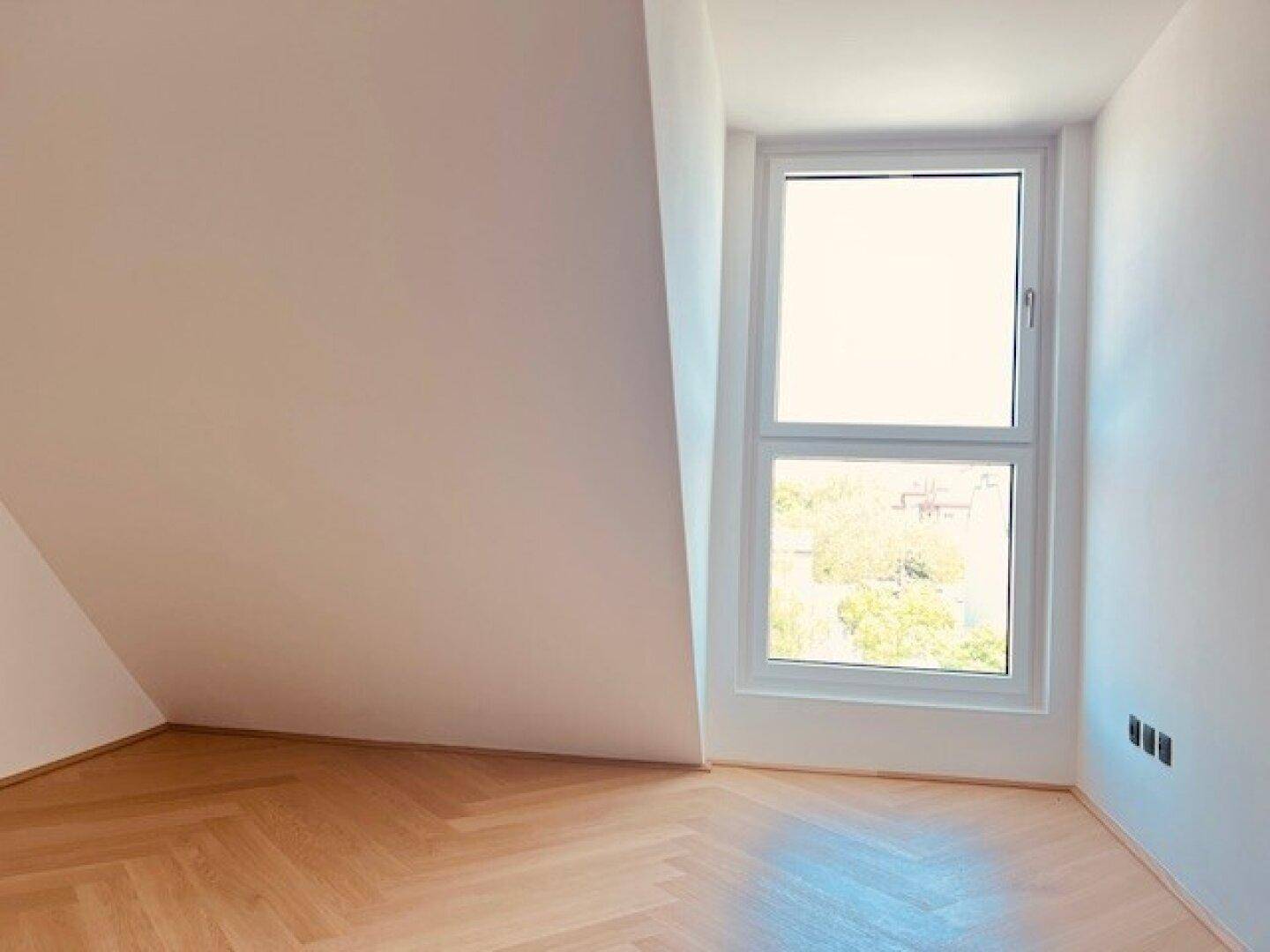 Helles Zimmer mit Fischgrätparkett und einem hohen Fenster, ideal für ein Schlafzimmer.