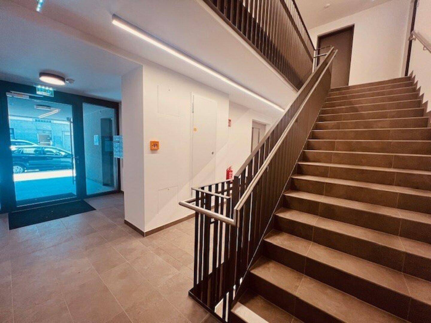 Moderner Eingangsbereich mit Treppenhaus, Fliesenboden und Zugang zu den Wohneinheiten.