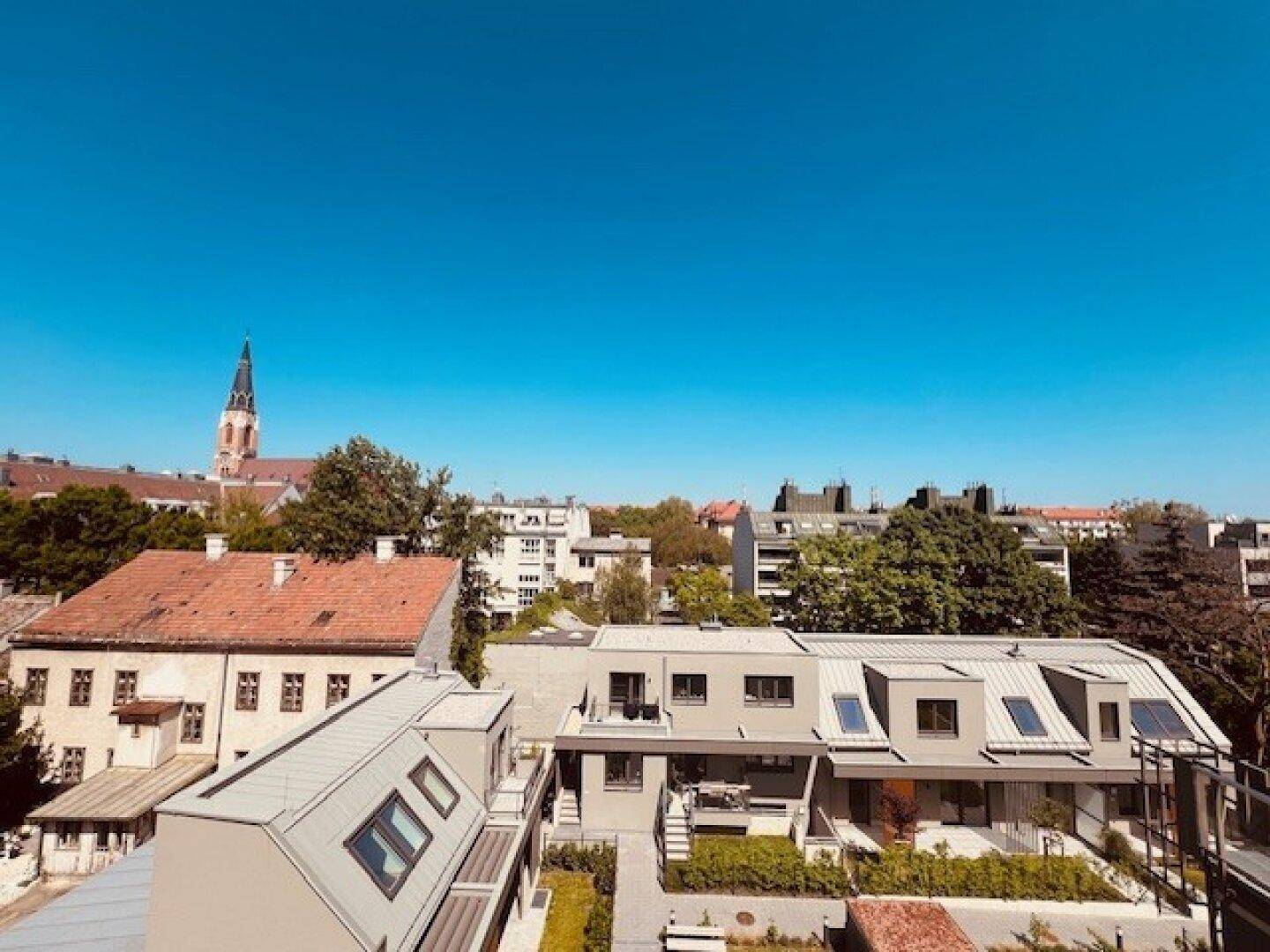 Weitläufiger Blick über eine städtische Dachlandschaft mit historischen Gebäuden und modernen Dächern.