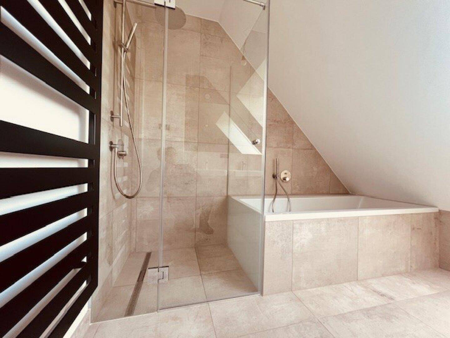 Elegantes Badezimmer mit begehbarer Dusche, Badewanne und beigefarbenen Fliesen unter Schrägdach.