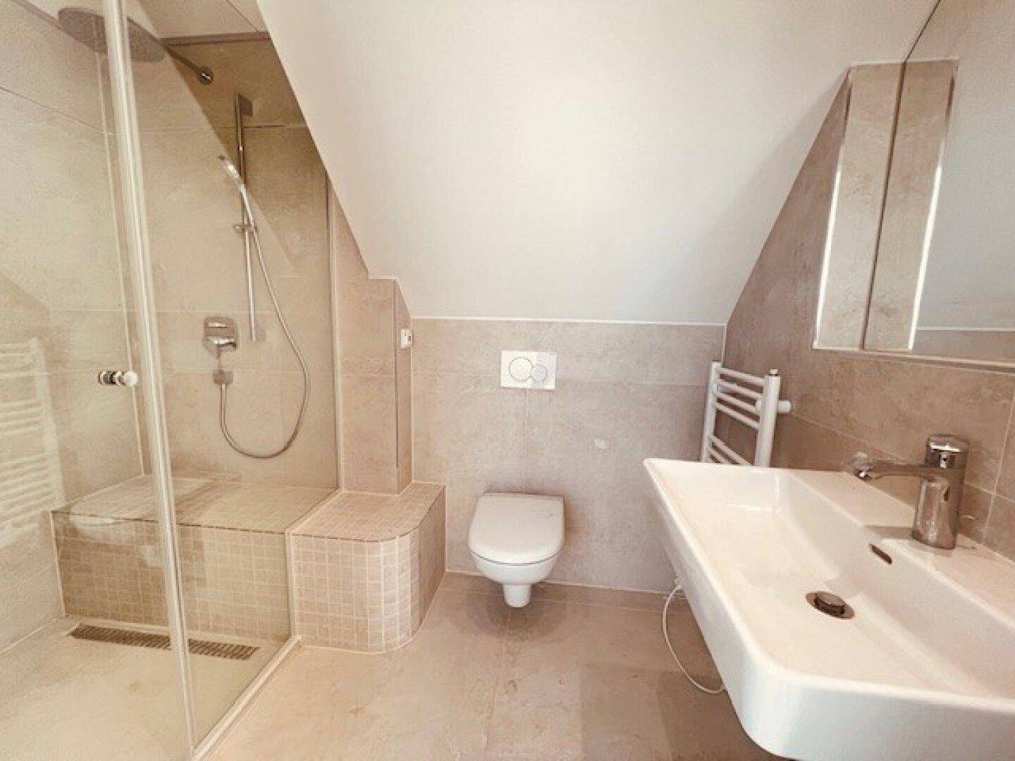 Modernes Badezimmer mit beigefarbenen Fliesen, begehbarer Dusche, Wand-WC und beheiztem Handtuchhalter.