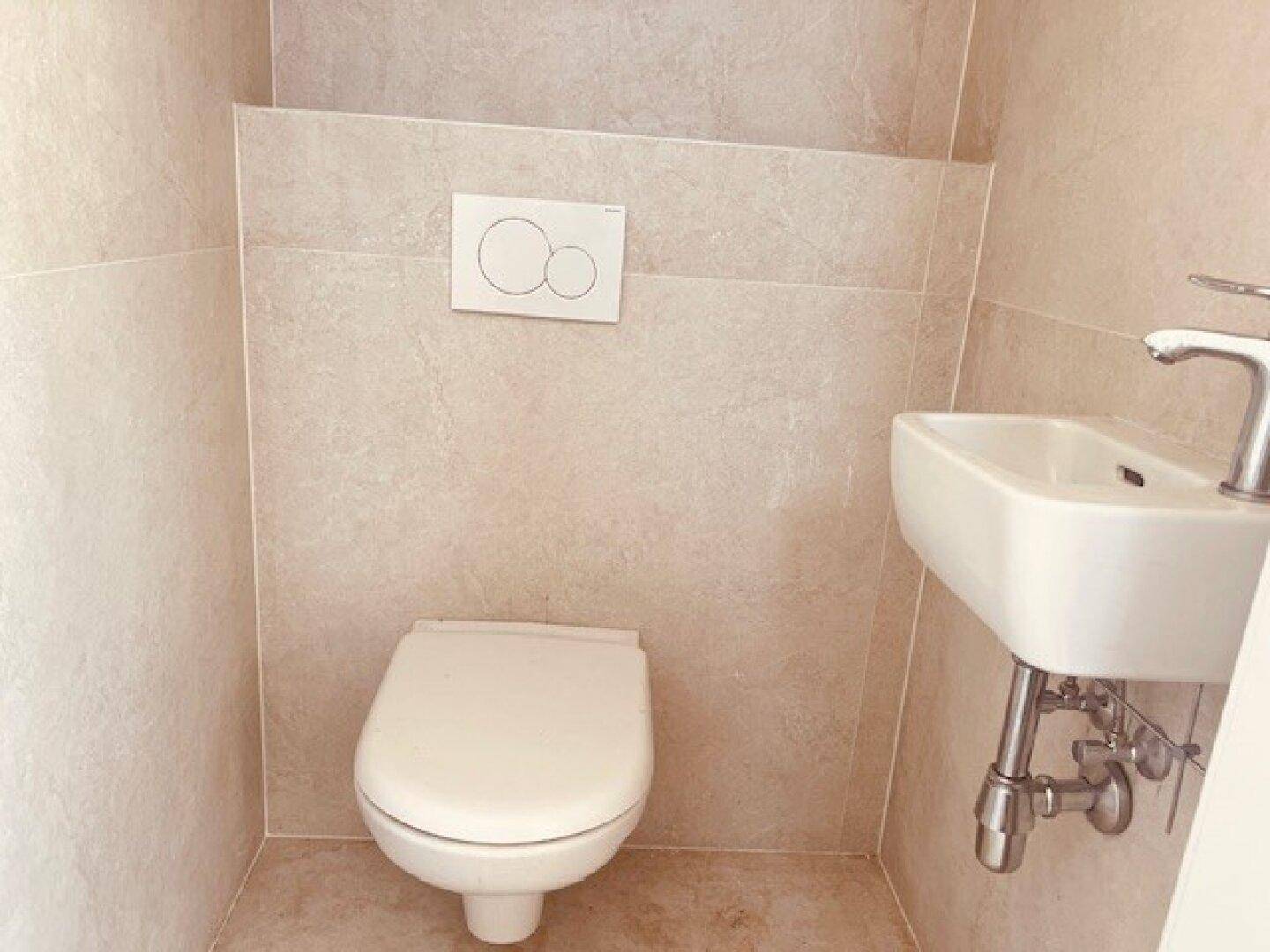 Kleines Gäste-WC mit beigefarbenen Fliesen, Wand-WC und kompaktem Waschbecken.