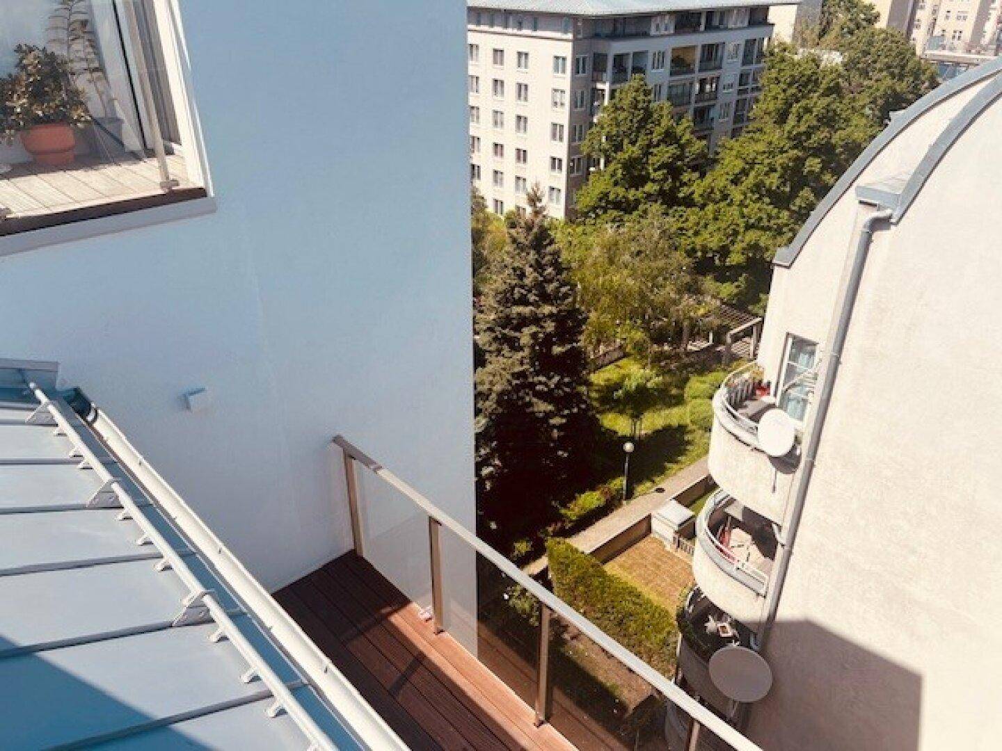 Blick von einem Balkon auf einen grünen Innenhof mit Bäumen und umliegenden Wohngebäuden.