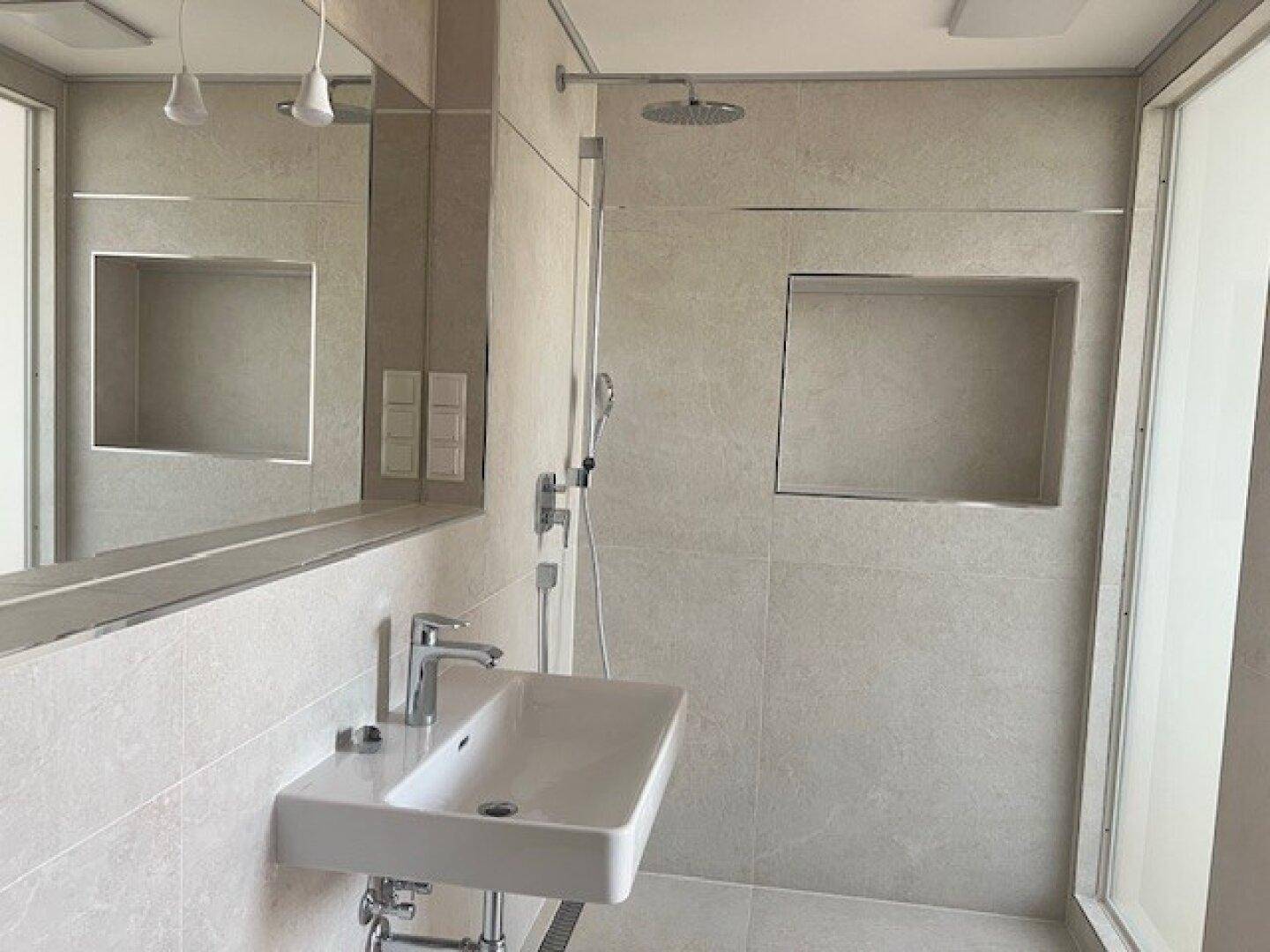 Elegantes Badezimmer mit moderner Dusche, Waschbecken und großem Spiegel, in hellen Fliesen gehalten.