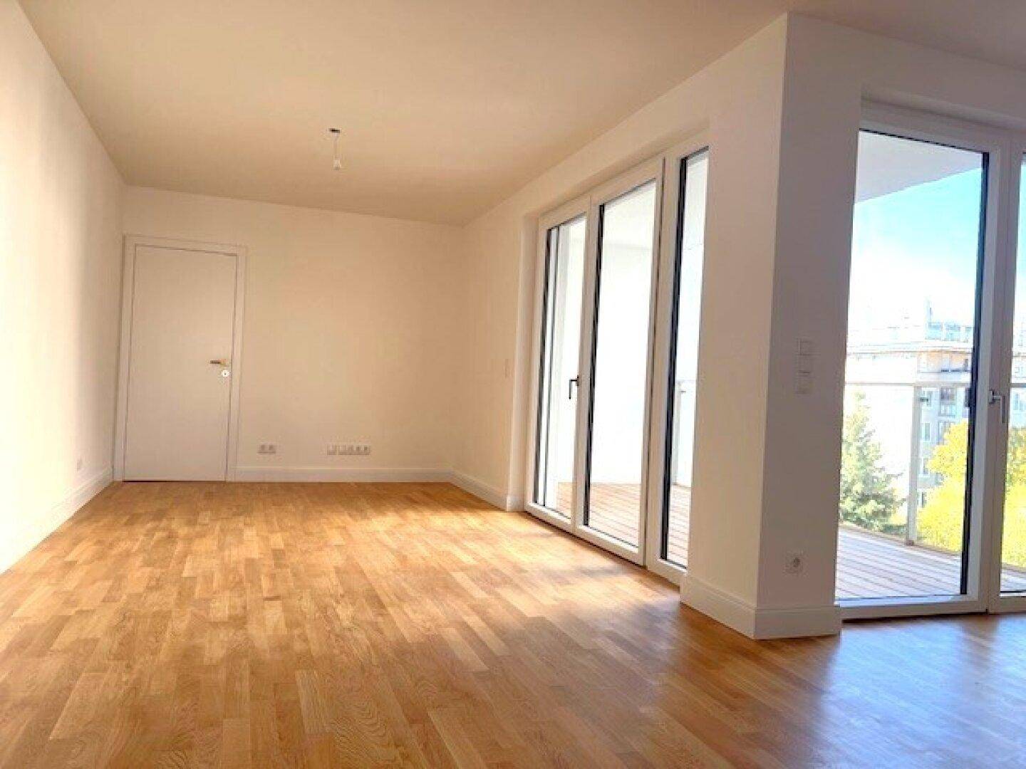 Geräumiges, leeres Zimmer mit Holzboden und großen Fenstern, die viel Licht hereinlassen.