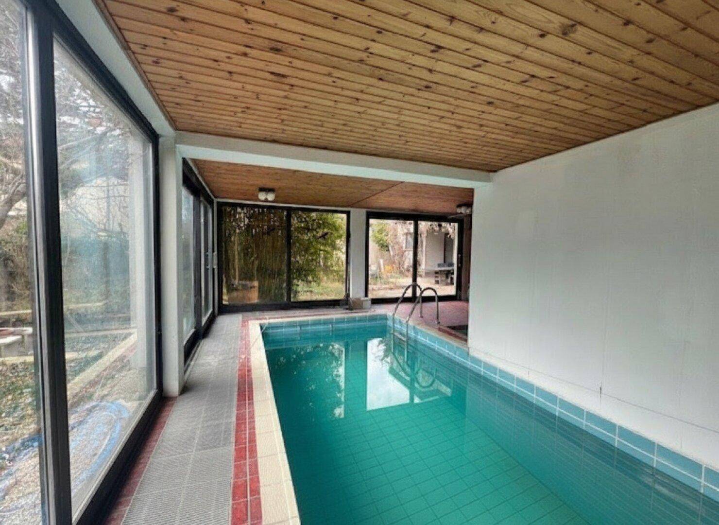 Innenpoolbereich mit großen Glasfronten, Holzdecke und Blick in den Garten.