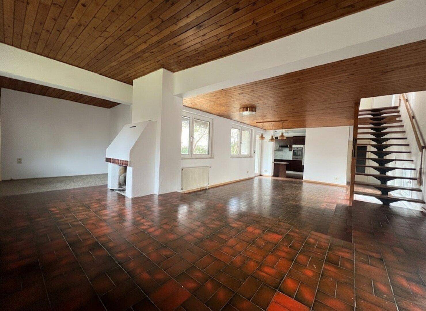 Geräumiges Wohnzimmer mit Terrakotta-Fliesenboden, Holzdecke, Kamin und offener Treppe.