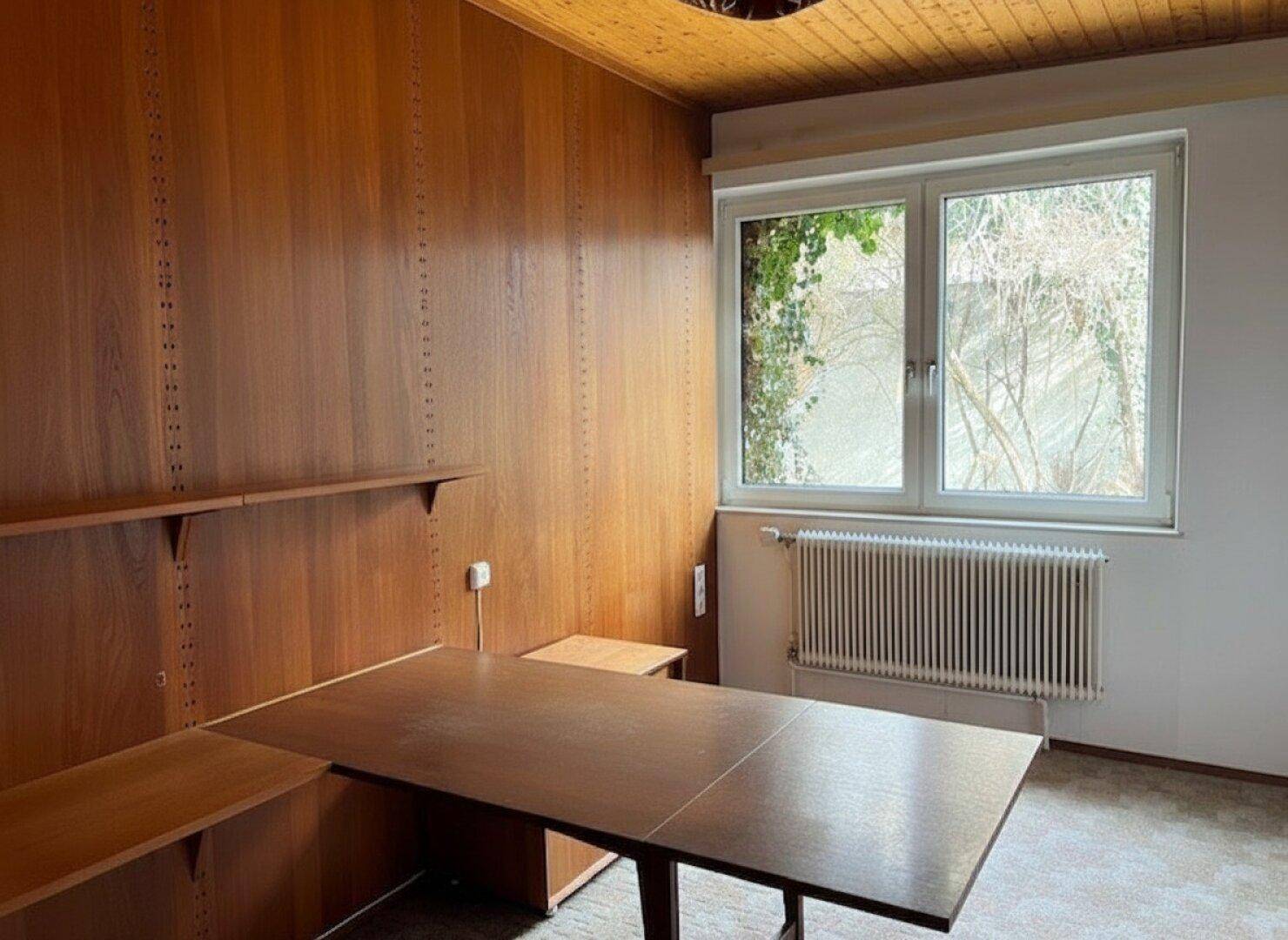 Zimmer mit Holzvertäfelung, großem Fenster und einem Schreibtisch, ideal als Arbeitszimmer.
