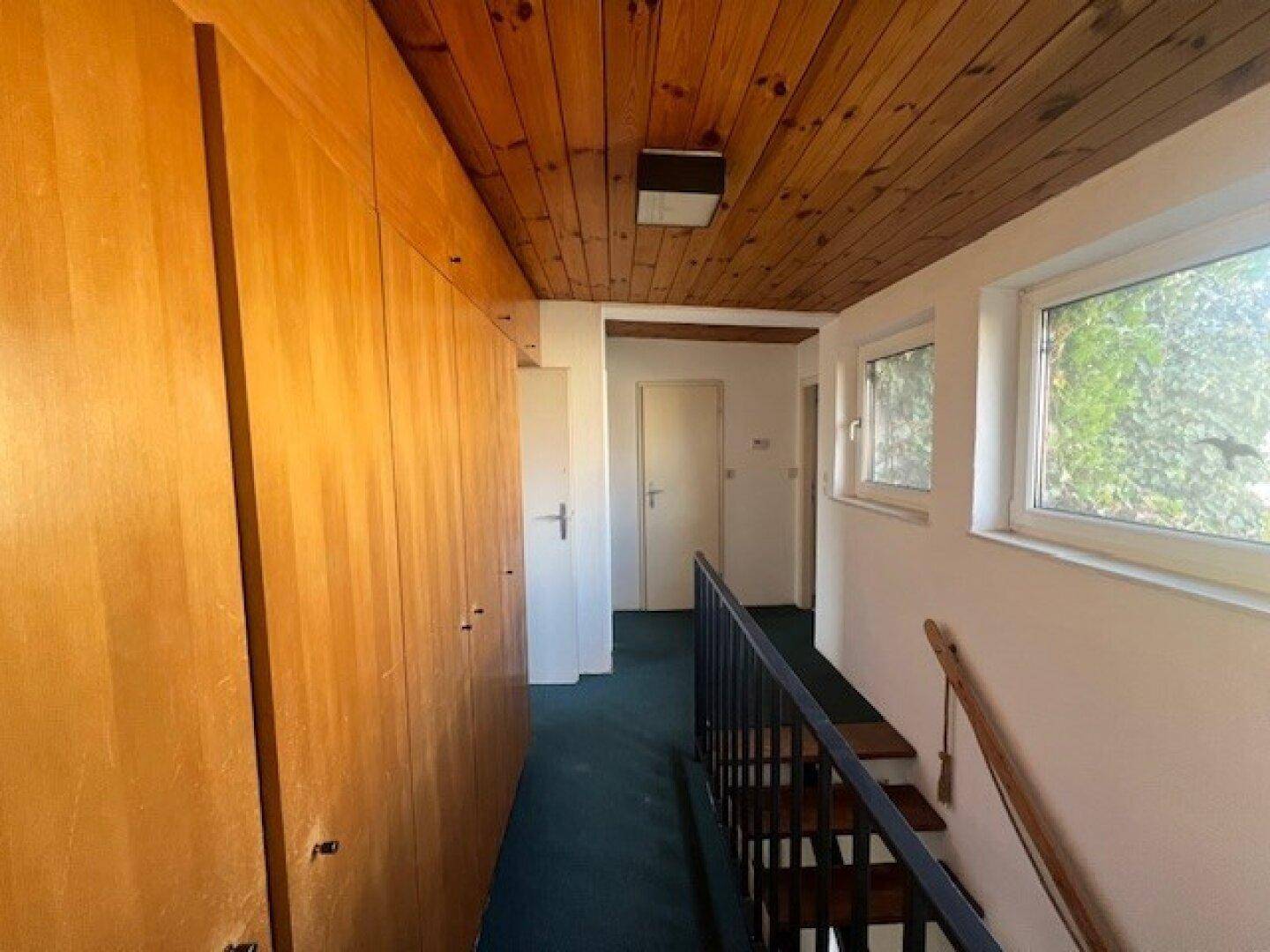 Flur im Obergeschoss mit Einbauschränken, Holzdecke und Blick ins Grüne durch die Fenster.