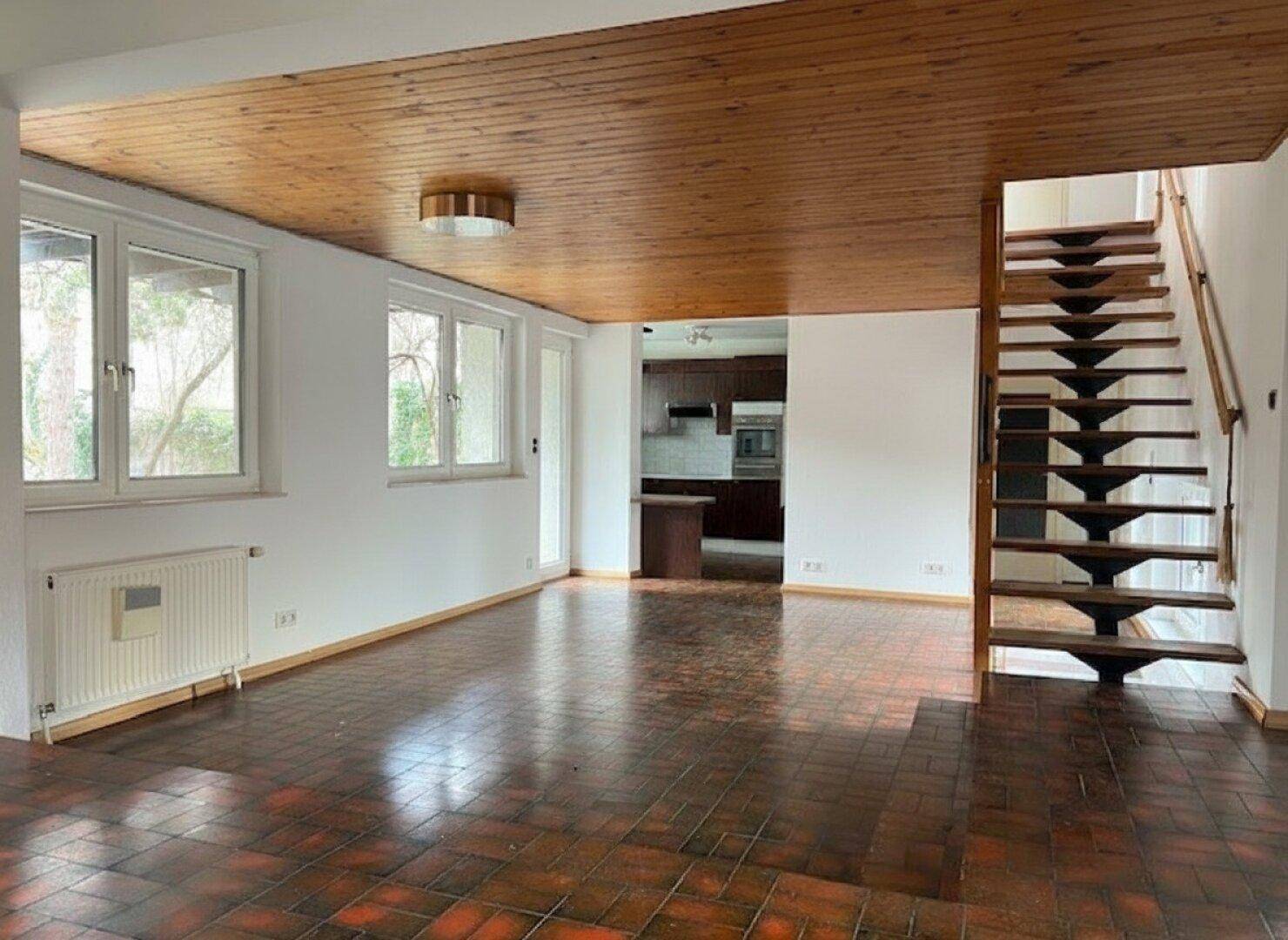 Heller Wohnbereich mit Terrakotta-Fliesenboden, Holzdecke und offener Treppe zum Obergeschoss.