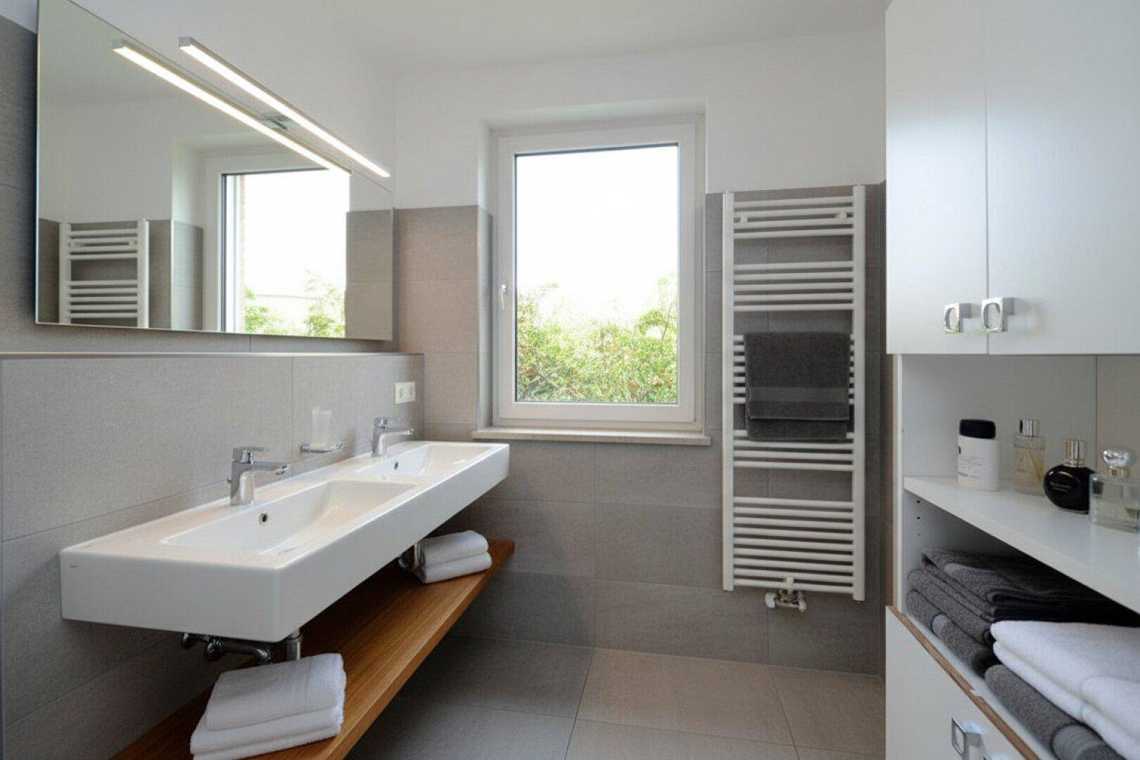 Modernes Badezimmer mit Doppelwaschbecken, großem Fenster und beheiztem Handtuchhalter.