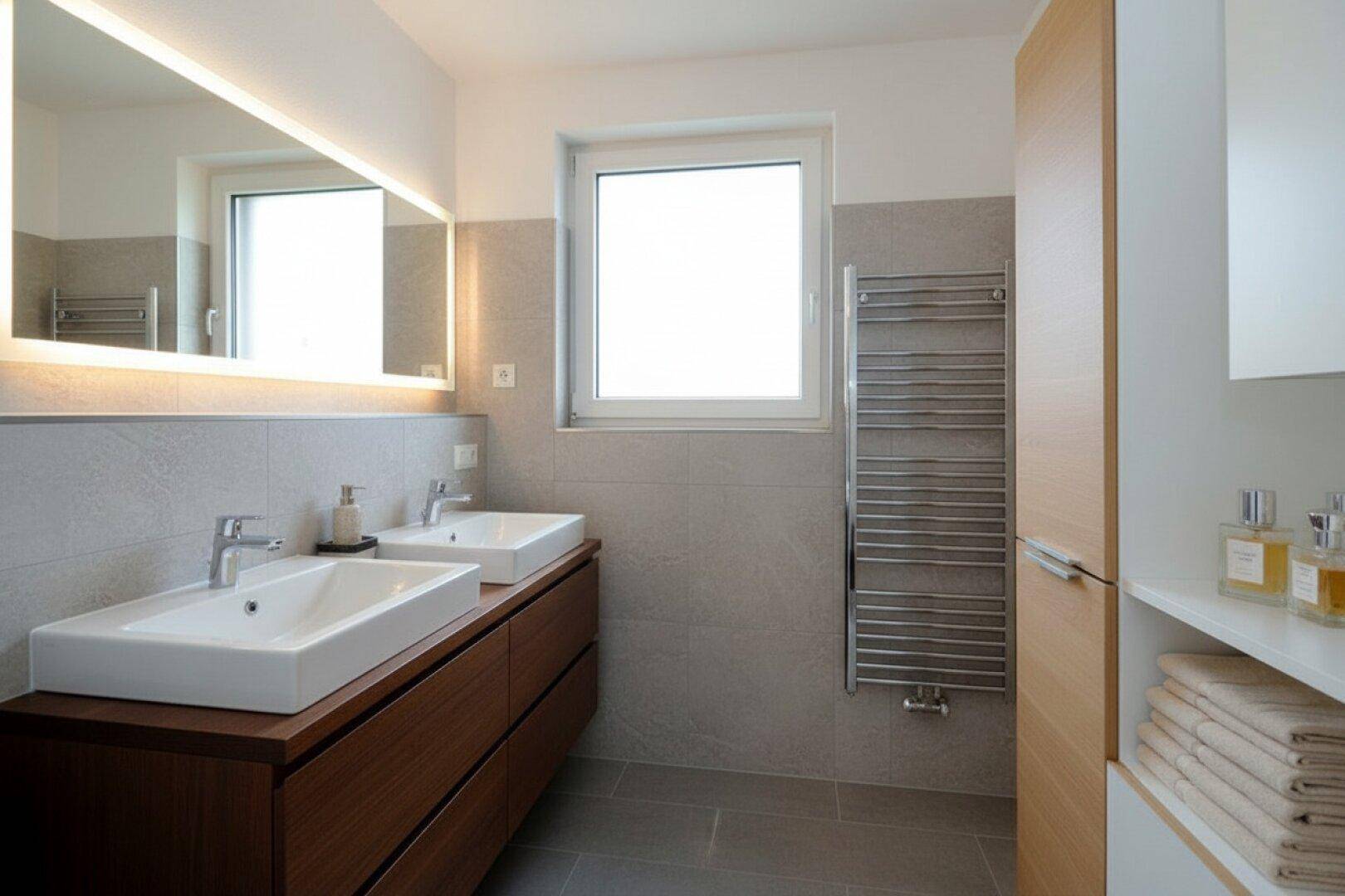 Modernes Badezimmer mit zwei Aufsatzwaschbecken, großem Spiegel und beheiztem Handtuchhalter.