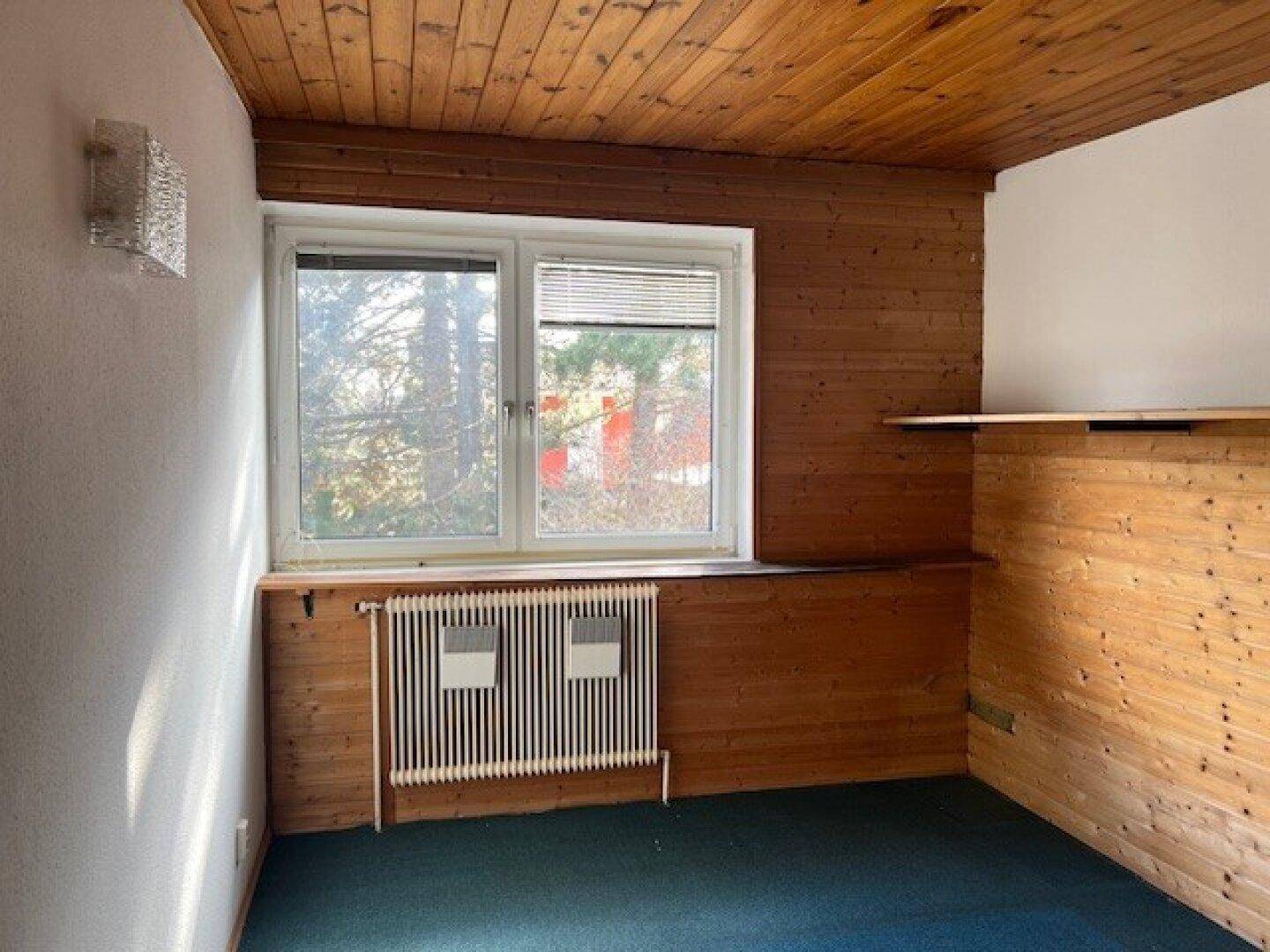 Schlafzimmer mit Holzvertäfelung, Teppichboden und großem Fenster, das viel Licht hereinlässt.