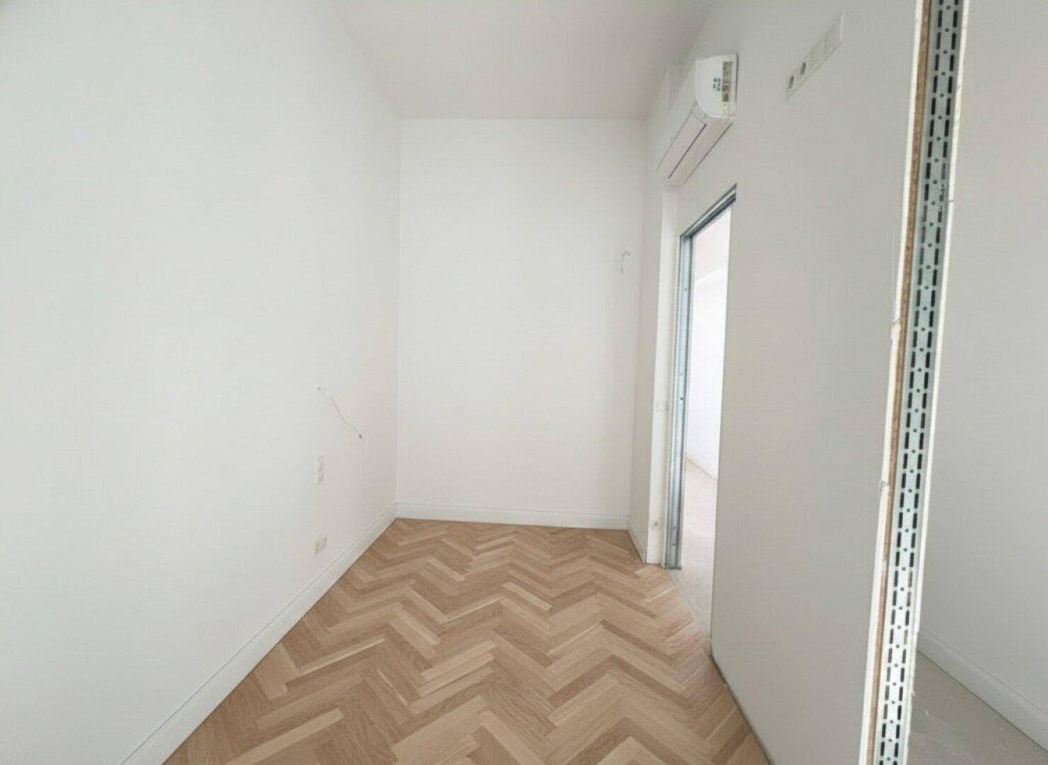 Kleiner, heller Raum mit Fischgrätparkett und Klimaanlage, ideal als Ankleide oder Kinderzimmer.