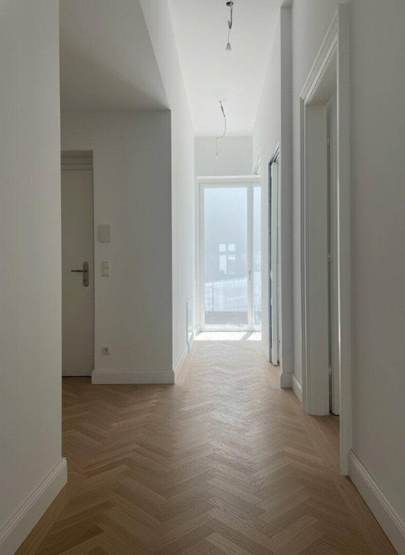 Langer, heller Flur mit Fischgrätparkett und einer Glastür, die viel Tageslicht hereinlässt.