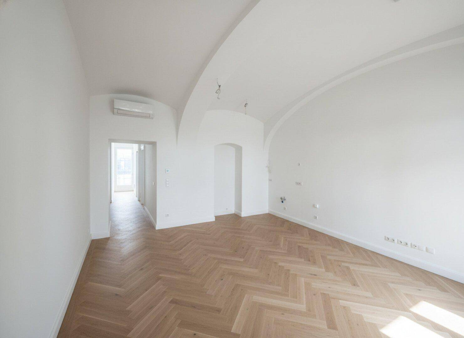 Heller Raum mit Fischgrätparkett, weißen Wänden und eleganten Gewölbedecken, bereit zur Einrichtung.