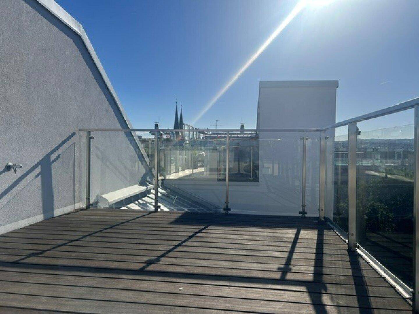 Geräumige Dachterrasse mit Glasgeländer und Holzboden, bietet einen weiten Blick über die Stadt.