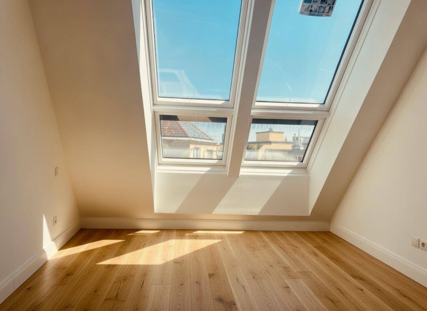 Lichtdurchfluteter Raum im Dachgeschoss mit schrägen Wänden und großen Dachfenstern, ideal für ein Schlafzimmer.
