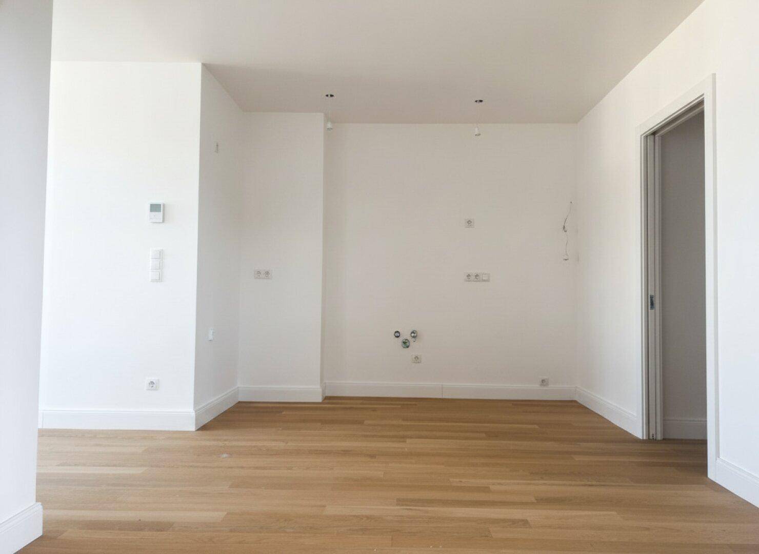 Leerer Küchenbereich mit Anschlüssen und Holzboden, bereit für die Installation einer modernen Einbauküche.