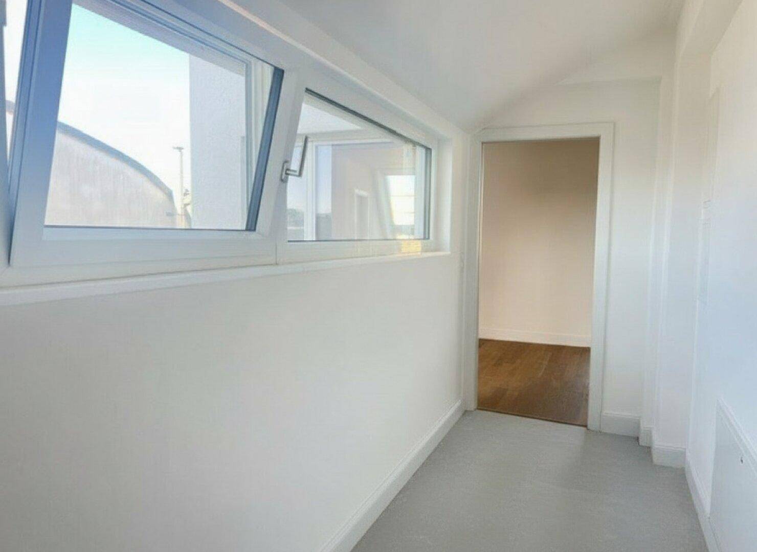 Heller Flur mit Fenster und hellem Boden, der zu weiteren Räumen führt.