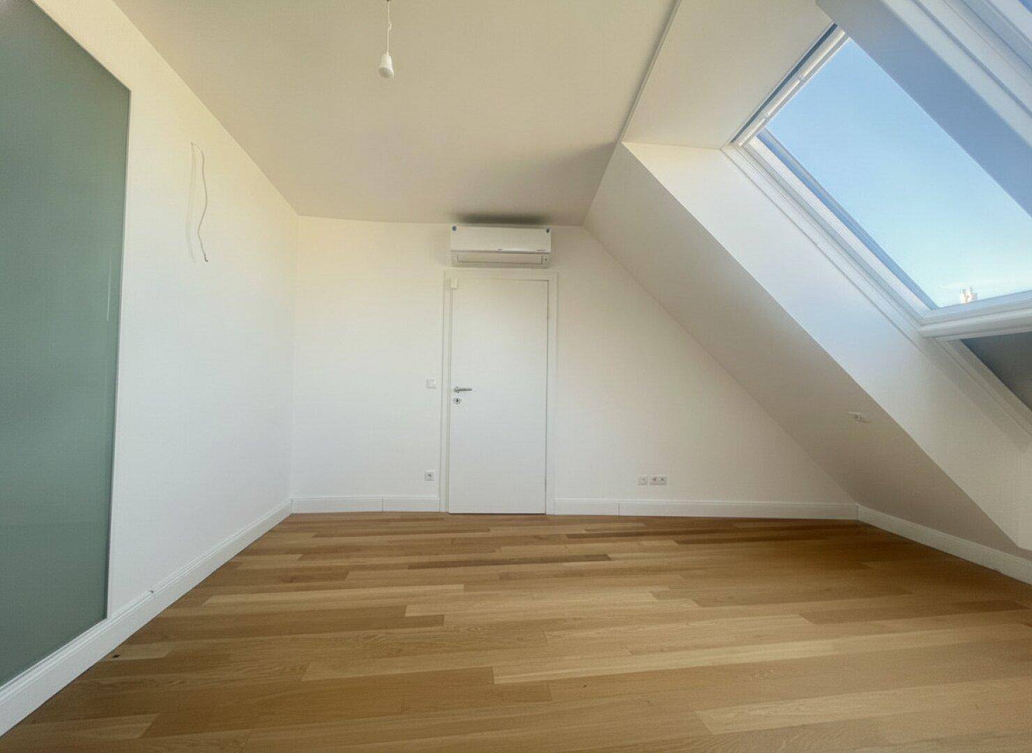 Helles Schlafzimmer im Dachgeschoss mit Holzboden, Dachfenster und einer Akzentwand in Grün.
