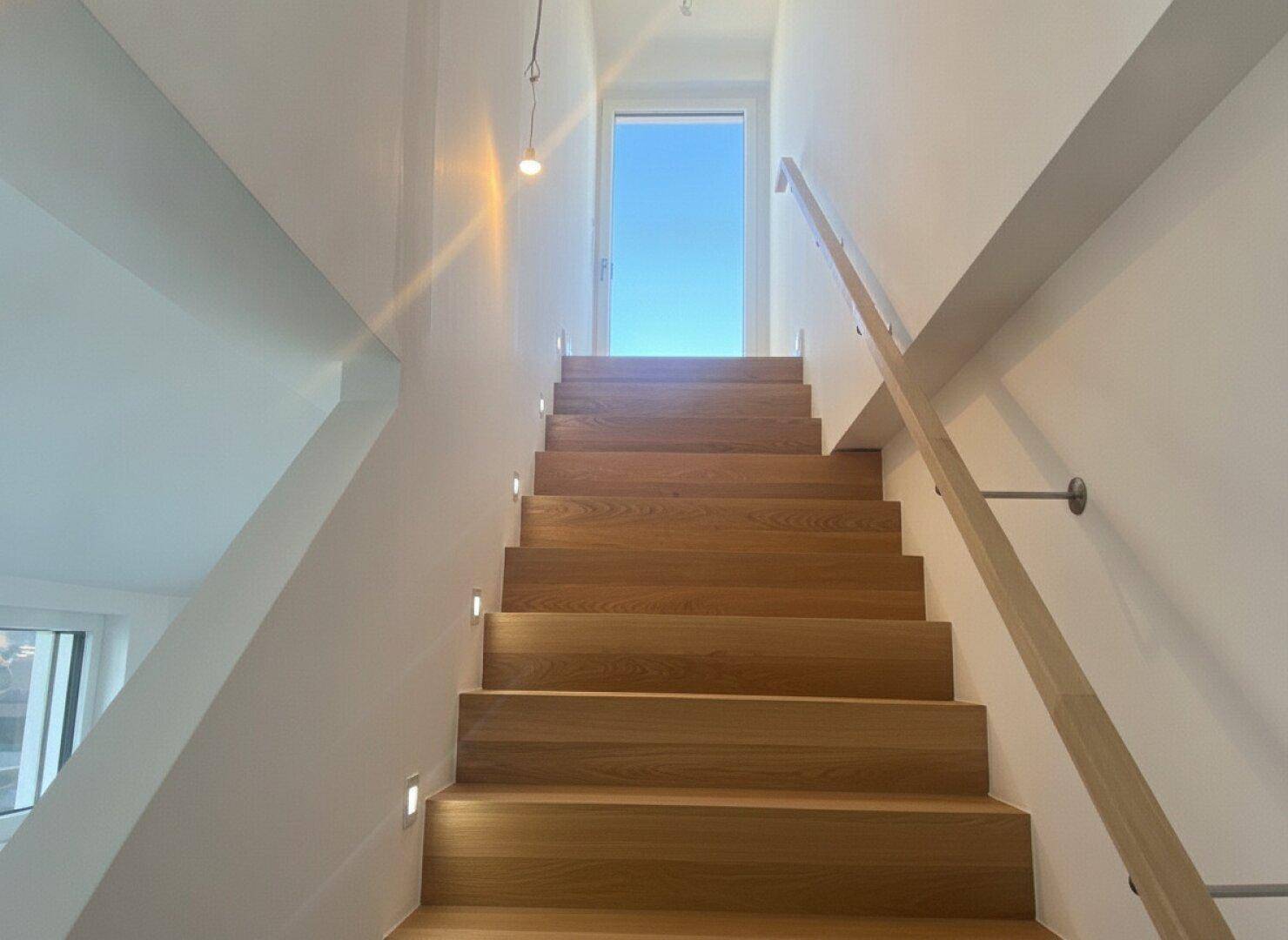 Moderne Holztreppe mit integrierter Beleuchtung und Handlauf, die zu den oberen Etagen führt.